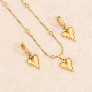 Golden heart pendant necklace and earrings set on minimalist textured warm background