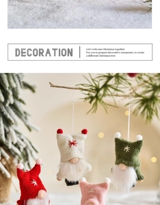 Close-up of colorful knitted Christmas gnomes hanging on pine branches with warm bokeh
