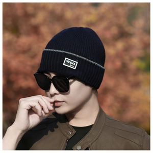 Detail of navy knit beanie with gray stripe and fashion label worn outdoors