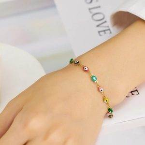Close-up of a gold chain bracelet featuring colorful enamel Evil Eye charms on a wrist