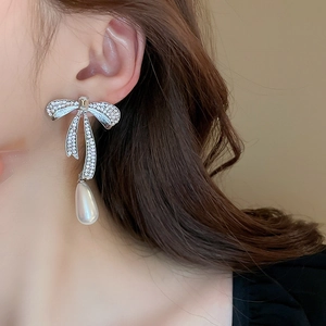 Detail of bow earrings featuring sparkling crystals and drop-shaped pearl on model