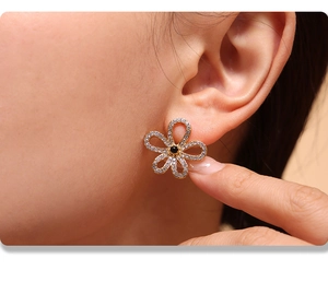 Close-up of golden flower earrings with clear crystals and a black gemstone center