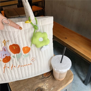 Close-up of white quilted tote bag featuring rabbit embroidery and green flower pendant