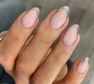 Macro shot of oval almond press-on nails with nude base and silver glitter V-French tips