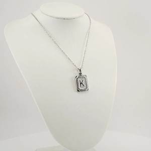 Detail of silver square pendant with letter K on a stainless steel curb chain