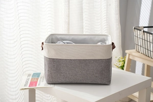Close-up of a two-tone linen storage basket with leather handles in a home setting