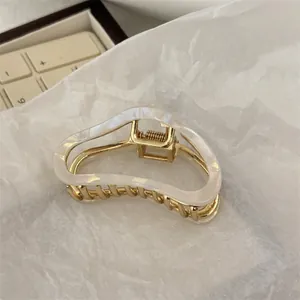 Detail of elegant wavy pearl white claw clip with pale gold metal frame for hair