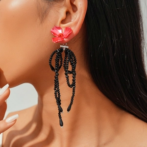 Detail of red flower stud earrings featuring long black beaded tassel on female model