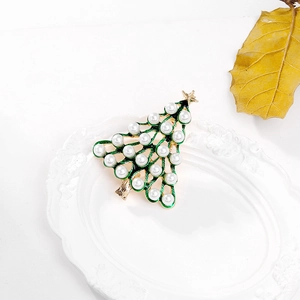 Detailed view of green enamel Christmas tree brooch with white pearls on white dish
