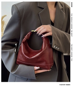 Detail of burgundy PU leather handbag with gold metal handle and embossed fashion logo