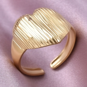 Gros plan d'une bague coeur dorée avec texture rayée verticale sur fond de soie