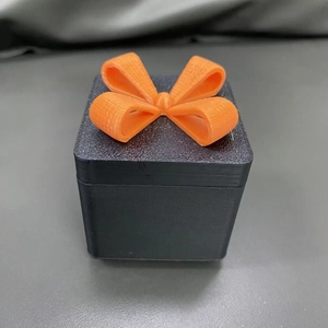 Dettaglio della scatola regalo stampata in 3D con fiocco arancione e trama plastica