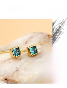 Macro shot of gold-plated square blue zircon earrings on a textured stone base