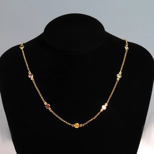 Close-up of colored round gemstones on a gold necklace displayed on black velvet