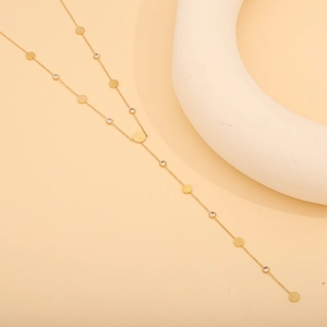 Detail of gold Y-shaped necklace with white zircon and round metal plates charms