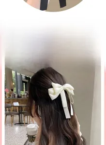 Detail of cream silk ribbon bow hair clip on long wavy hair with long flowing streamers