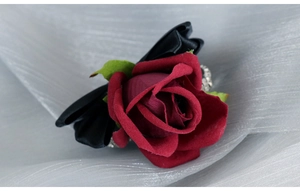 Close-up of deep red velvet rose boutonniere with black satin bow and green leaves