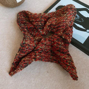 Détail d'un chouchou en tweed rouge et noir avec des fils dorés sur une surface texturée