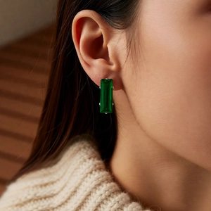 Close-up of emerald green zircon square stud earrings worn with a beige knit sweater