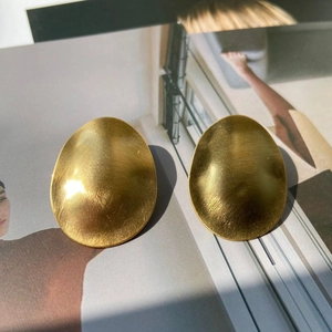 Detail of gold oval earrings with brushed matte texture and minimalist metallic finish