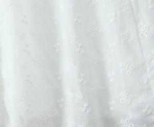 Detailed macro view of white floral embroidery and vine patterns on woven fabric