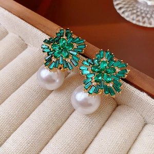 Detail of flower-shaped green crystal and white pearl earrings in a beige velvet jewelry box