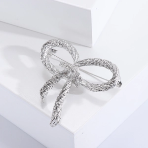 Macro view of silver bow brooch with rope texture detail on white geometric display