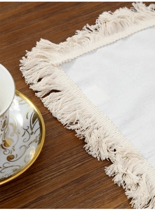 Detail of white cotton linen placemat with fringe on a dark wood table