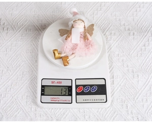 Detail shot of a plush pink Christmas angel ornament with golden wings on a digital scale