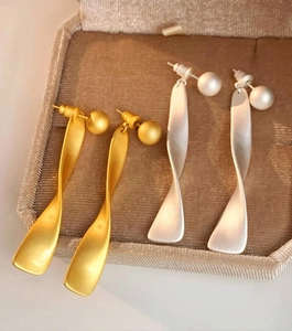 Detail view of irregular twisted metal drop earrings with matte brushed finish in gold and silver