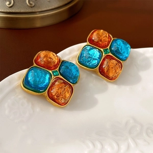 Detail of vintage square stud earrings with blue and orange stones on a white ceramic plate