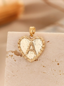 Macro shot of gold heart pendant with letter A on textured stone background