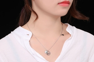 Detailed close-up of a silver Peace pendant necklace with sparkling rhinestones on a neck