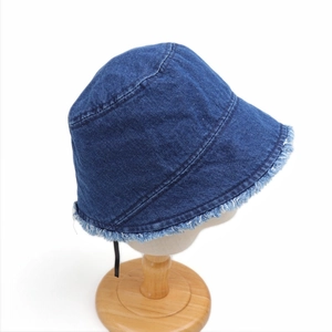 Detailed view of dark blue denim bucket hat with frayed edges on a wooden stand