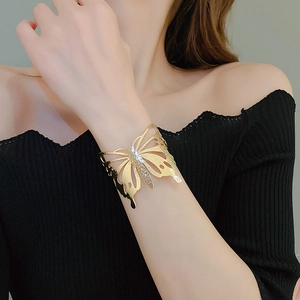 Close-up of oversized golden butterfly cuff bracelet on model's arm with black top
