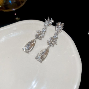 Macro view of crystal drop earrings with leaf motifs on a ceramic tray over black background