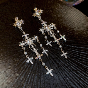Close-up of gothic cross earrings with sparkling crystals and white pearl tassels