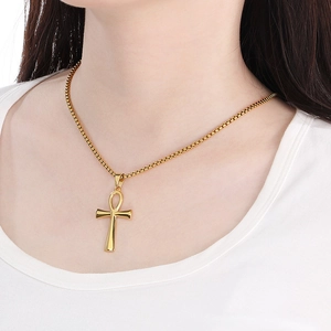 Close-up of a gold Ankh cross pendant necklace worn by a model on a white shirt
