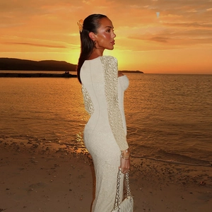 Eng anliegendes weißes Spitzenkleid mit langen Ärmeln vor einem Strand bei Sonnenuntergang