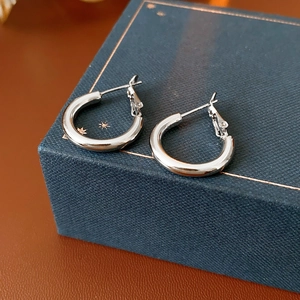 Minimalist silver hoop earrings presented on a dark blue textured jewelry box