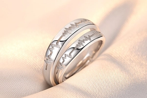 Detailed close-up of silver couple rings featuring heartbeat wave engraving on beige silk