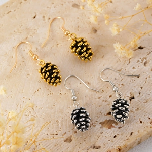 Detail of pinecone drop earrings in gold and antique silver finish on a stone base