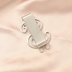Detailed view of matte silver dollar sign money clip on soft pink silk background