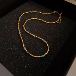 Détail macro d'un collier choker doré en acier inoxydable avec perles bleues en coffret