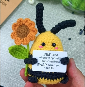 Macro shot of handmade crochet bee plush holding a sunflower with positive quote tag