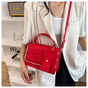 Detail of red crocodile pattern handbag with white wavy edges and gold buckle