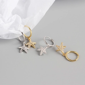 Macro shot of gold and silver starfish hoop earrings with zircon stones on a grey base