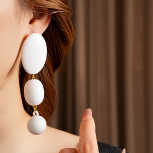 Close-up of elegant long earrings featuring three white oval beads and gold ring links