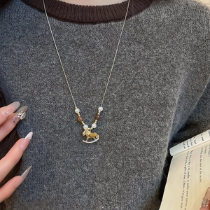 Detail of a gold rocking horse necklace with tiger eye stone and pearls on a sweater
