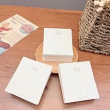 Three stacks of white rectangular jewelry display cards with handmade bow design on wood